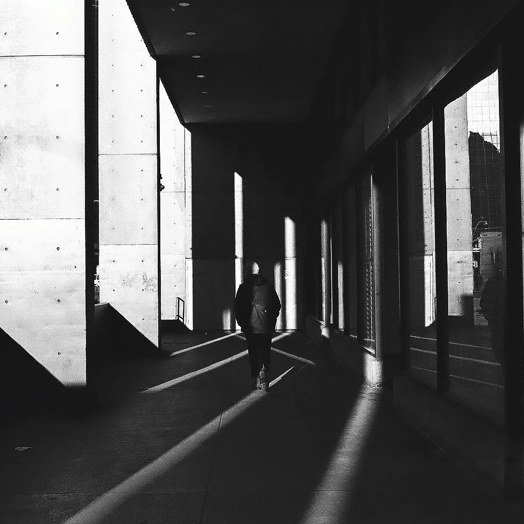A black and white photo of a man walking in geometric shadows