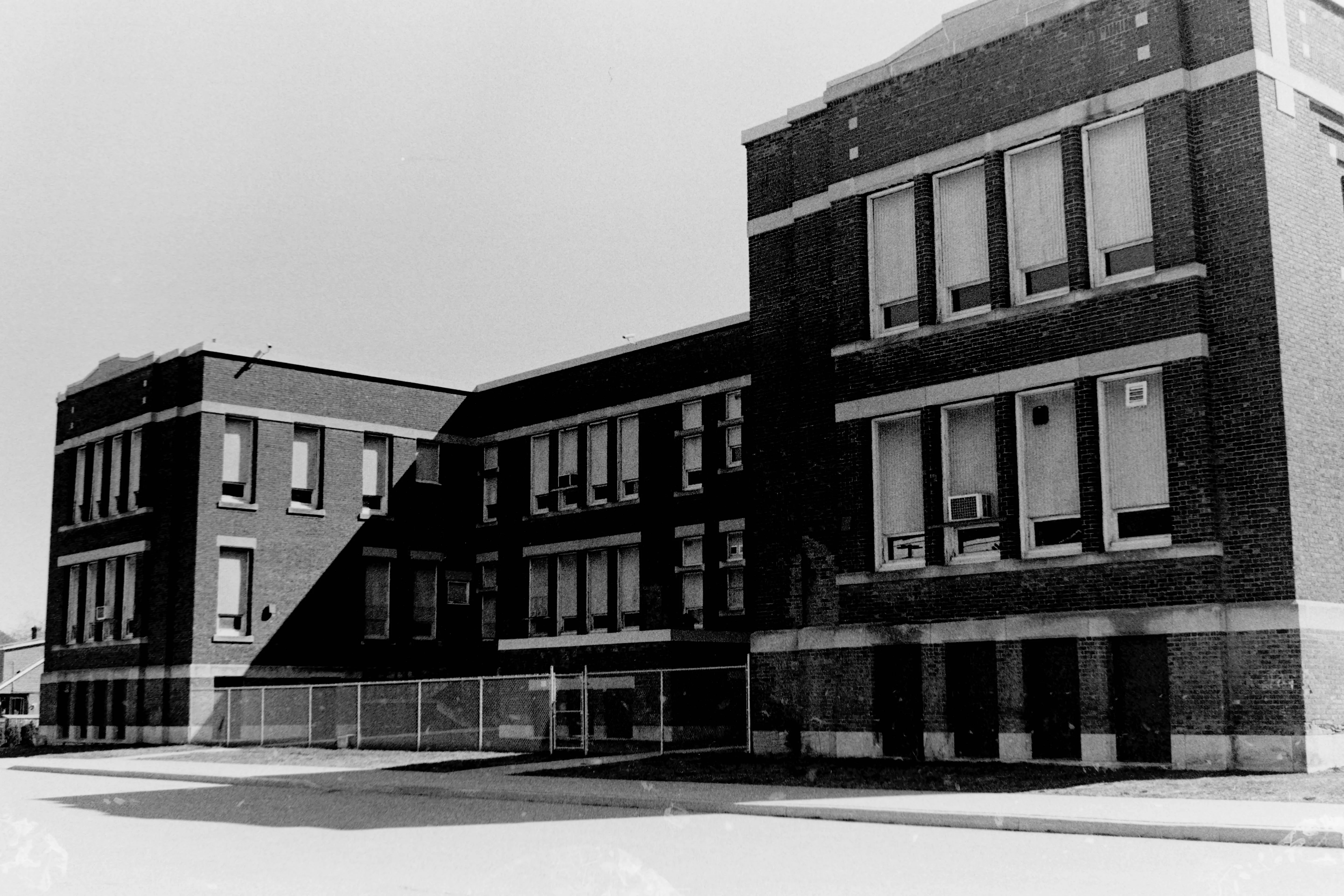 A black and white photo of an old school with strong shadows.