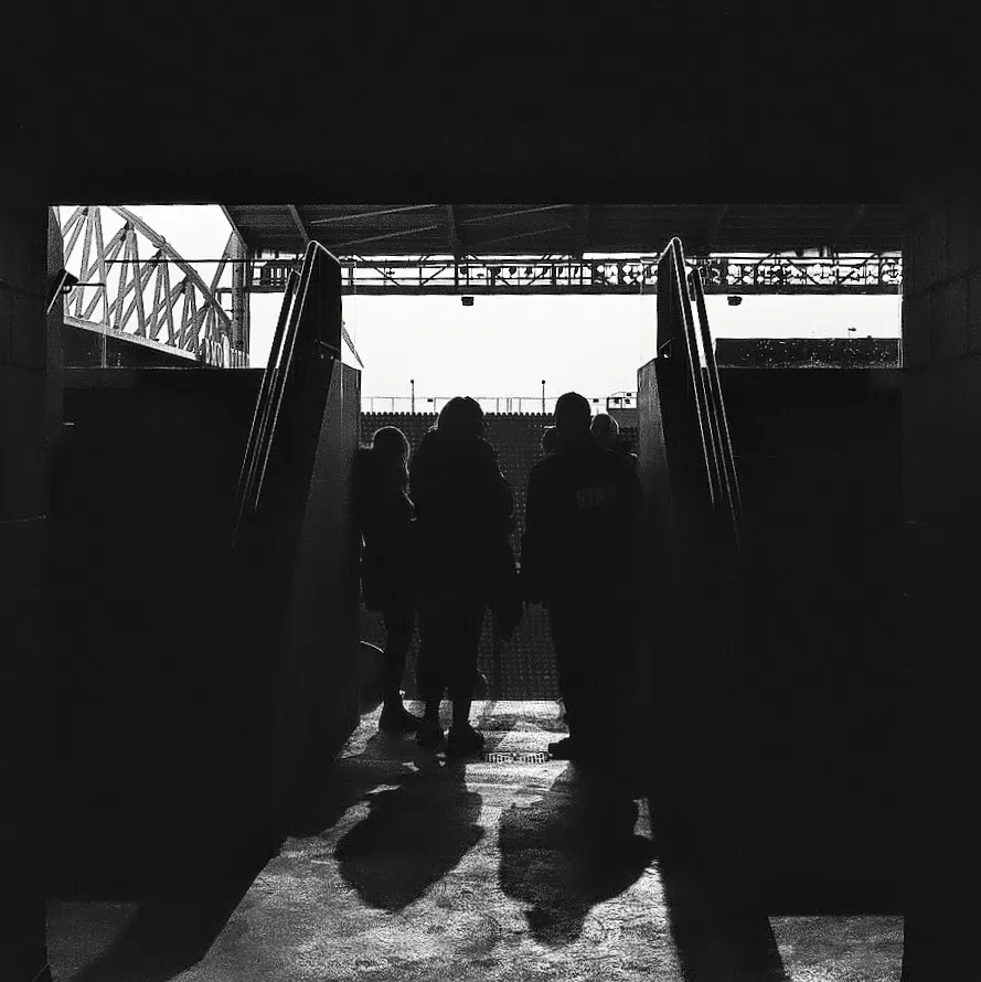 High contrast black and white photo of 4 people's silhouette stand at the entrance of stadium seating.